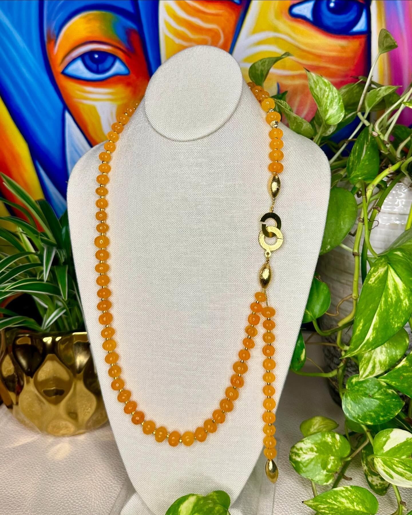 White textured necklace display with amber bead necklace, gold accents, and green leaves against colorful faces backdrop