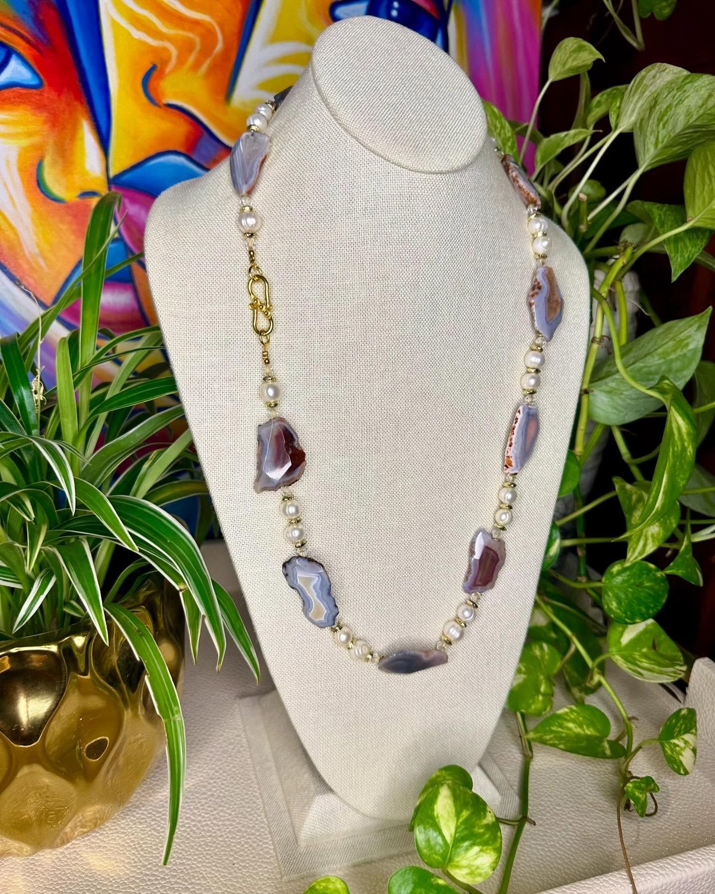 Beaded necklace displayed on a white mannequin bust, surrounded by green plants and colorful decor.