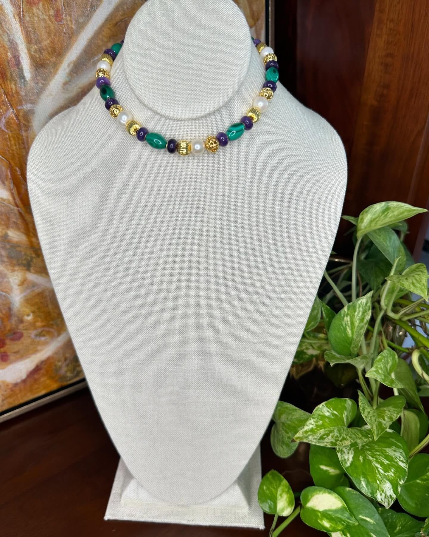 White textured necklace bust displaying a multicolored beaded necklace, with a green houseplant beside it.