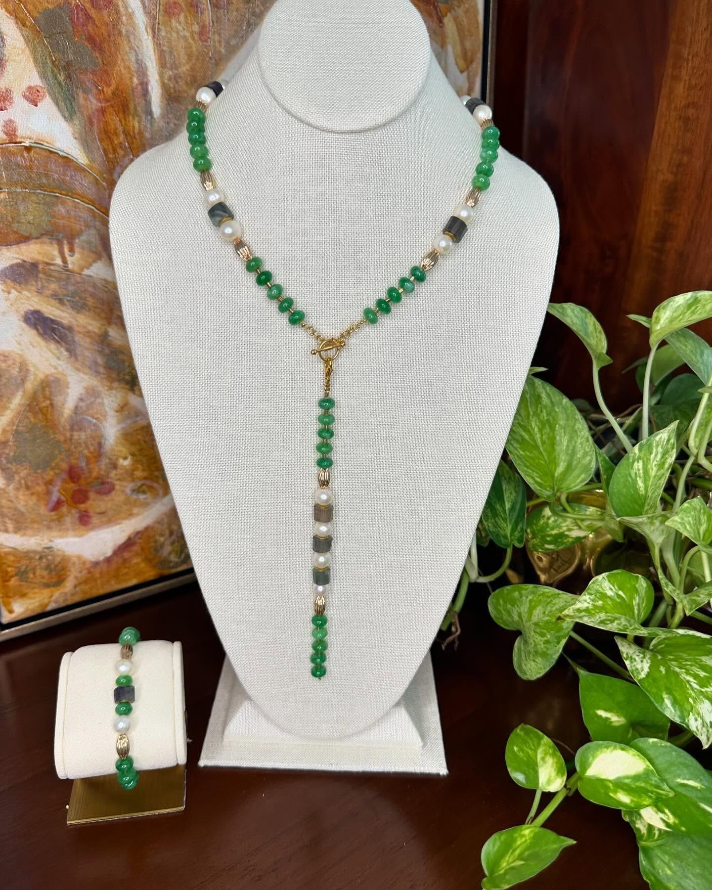 Green and silver beaded necklace displayed on a white bust, with matching bracelet on a small stand.