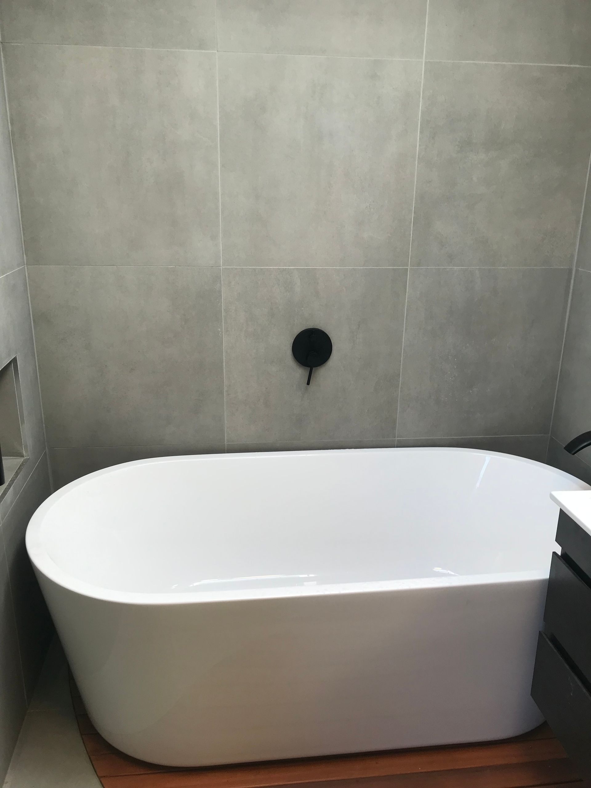White freestanding bathtub against gray tiled bathroom wall with a black wall fixture White freestanding bathtub against gray tiled bathroom wall with a black wall fixture