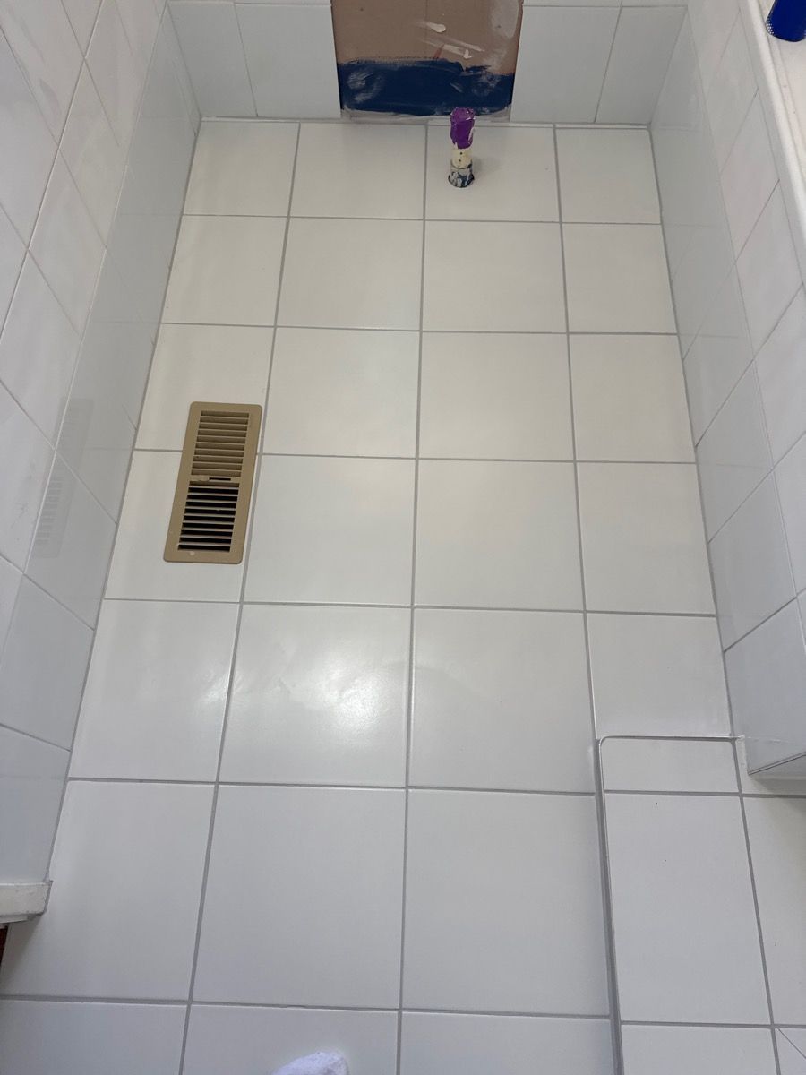 Tiled bathroom floor with a vent, toilet paper roll, and a bottle near the wall. Tiled bathroom floor with a vent, toilet paper roll, and a bottle near the wall.