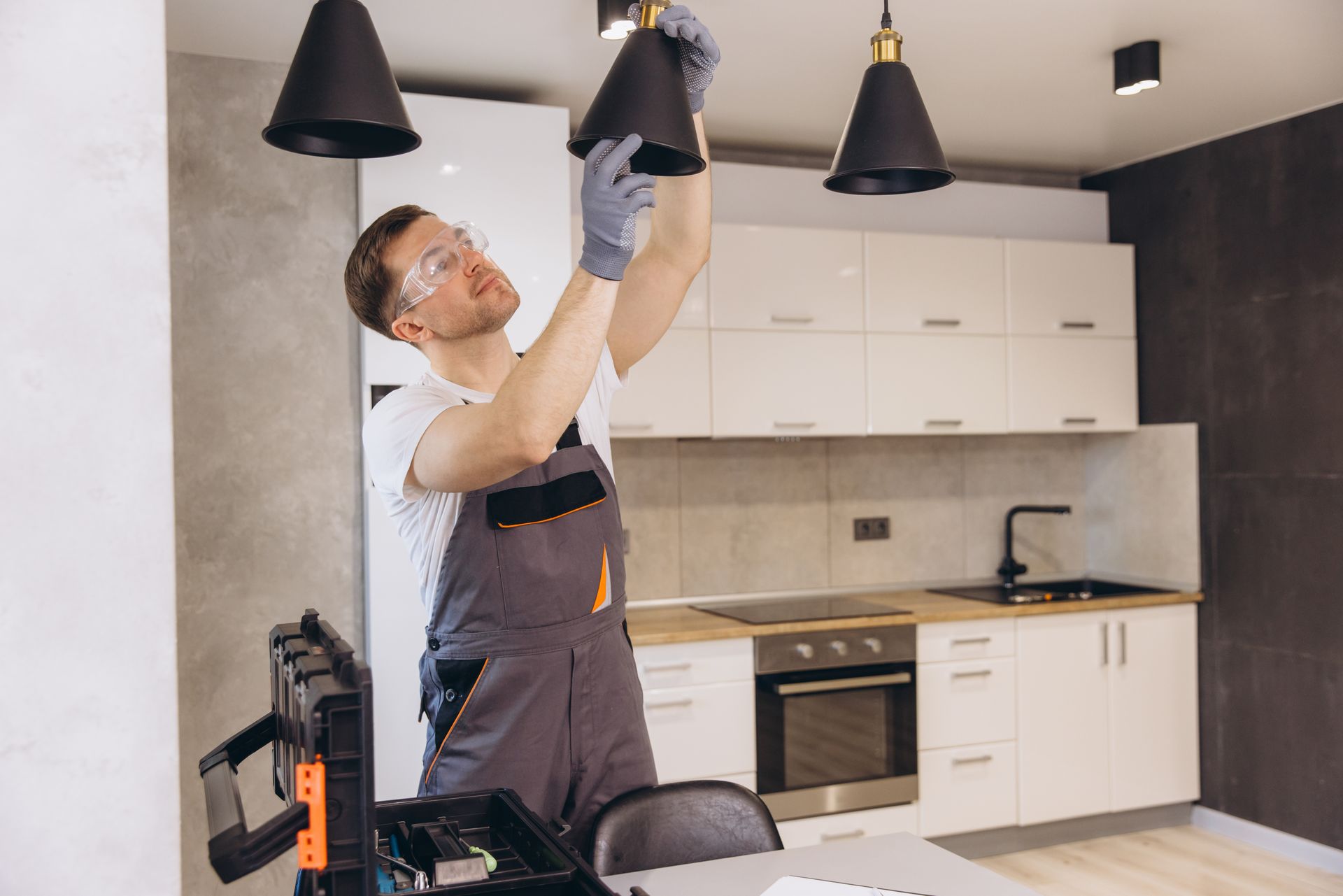 Man in coveralls installing a black pendant light in a kitchen.