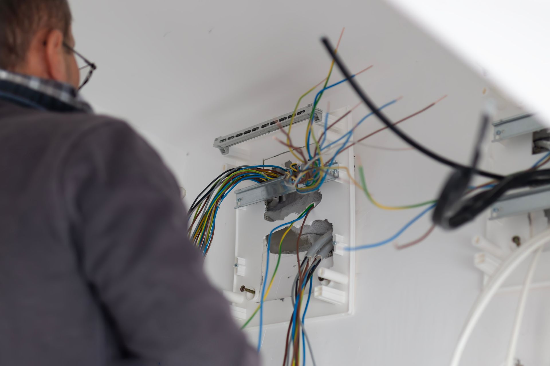Person working on exposed electrical wiring in a white junction box. Wires are blue, yellow, and green.