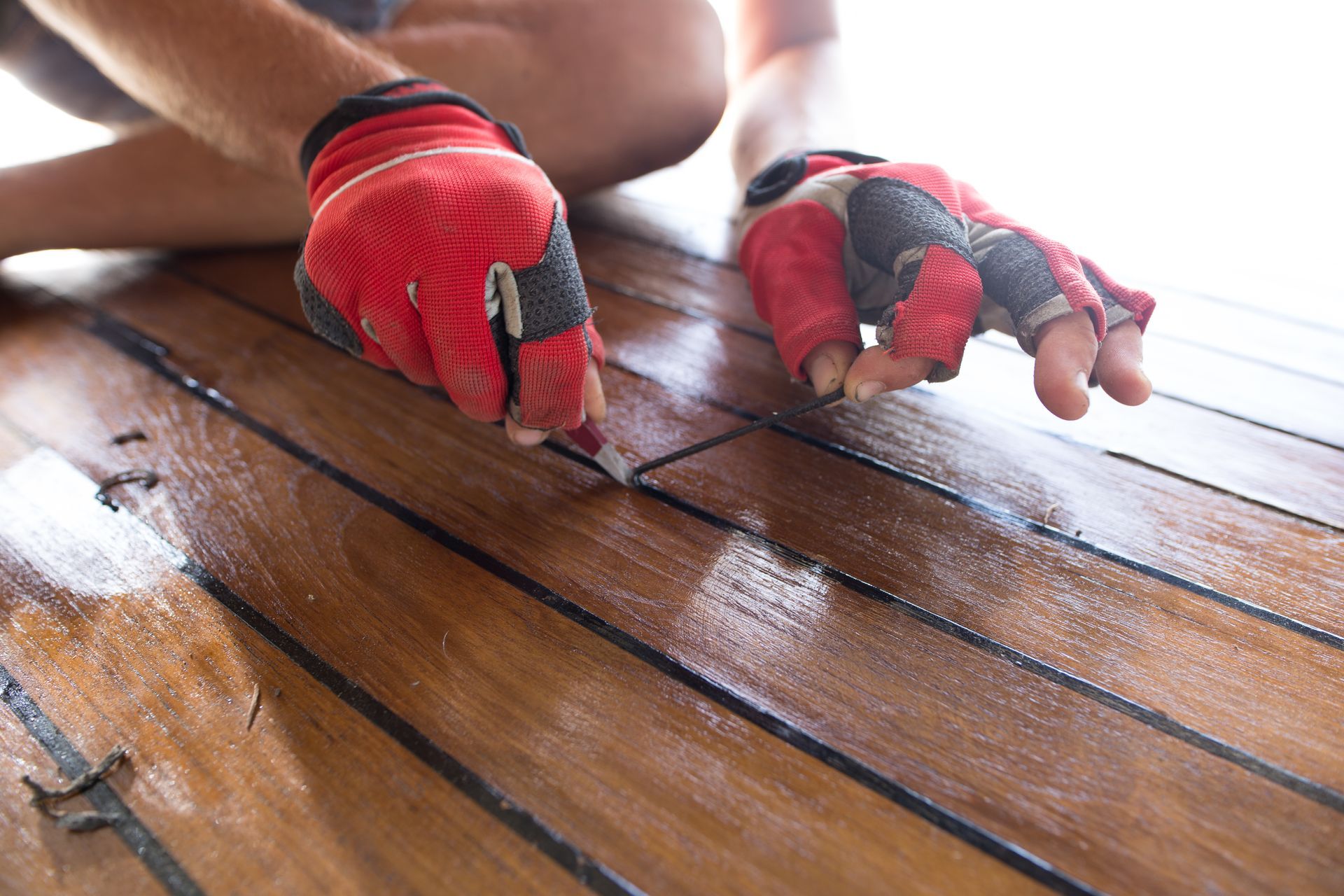 Person using gloved hands to apply sealant to teak decking on a boat.