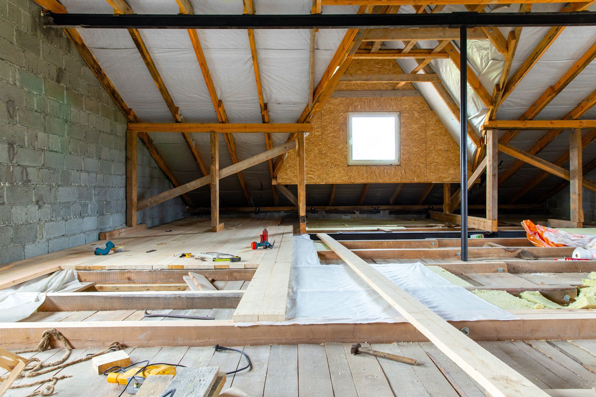 Attic under construction, showing exposed wooden beams, insulation, and building materials.