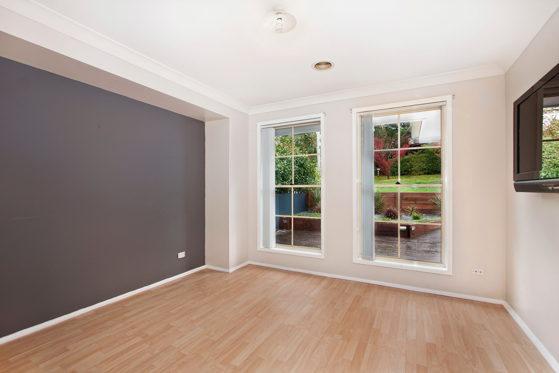 Empty room with wood floors, dark gray accent wall, two windows, and mounted television.