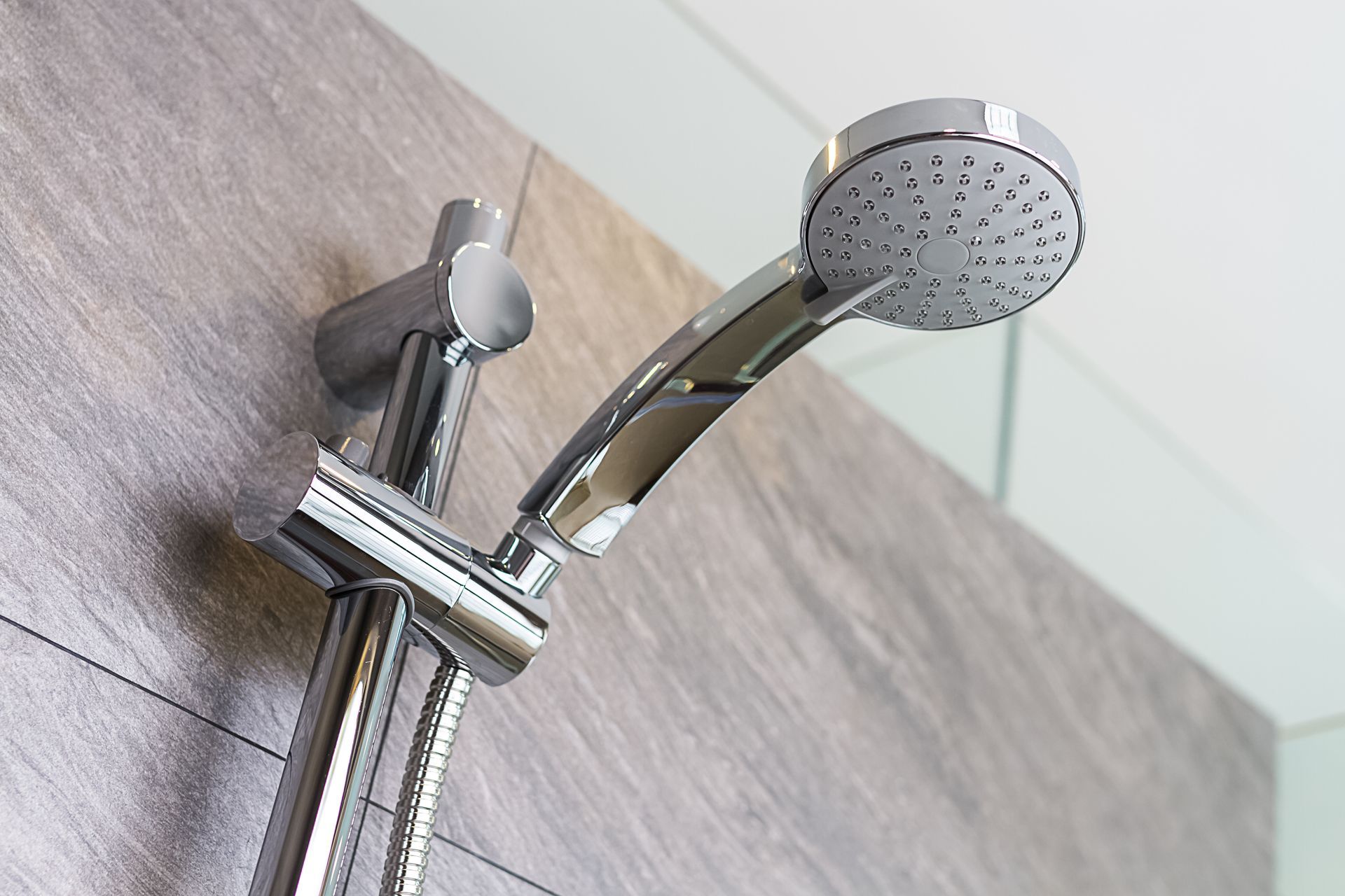 Chrome showerhead mounted on a gray tiled wall.