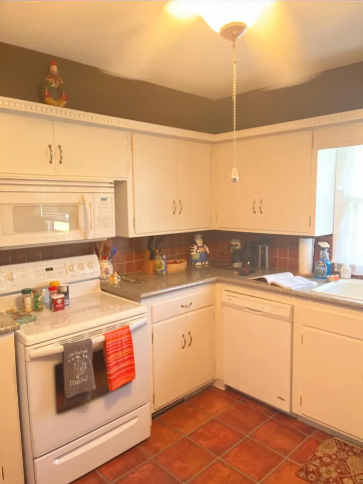 A kitchen with white cabinets , a stove , a microwave , and a sink.