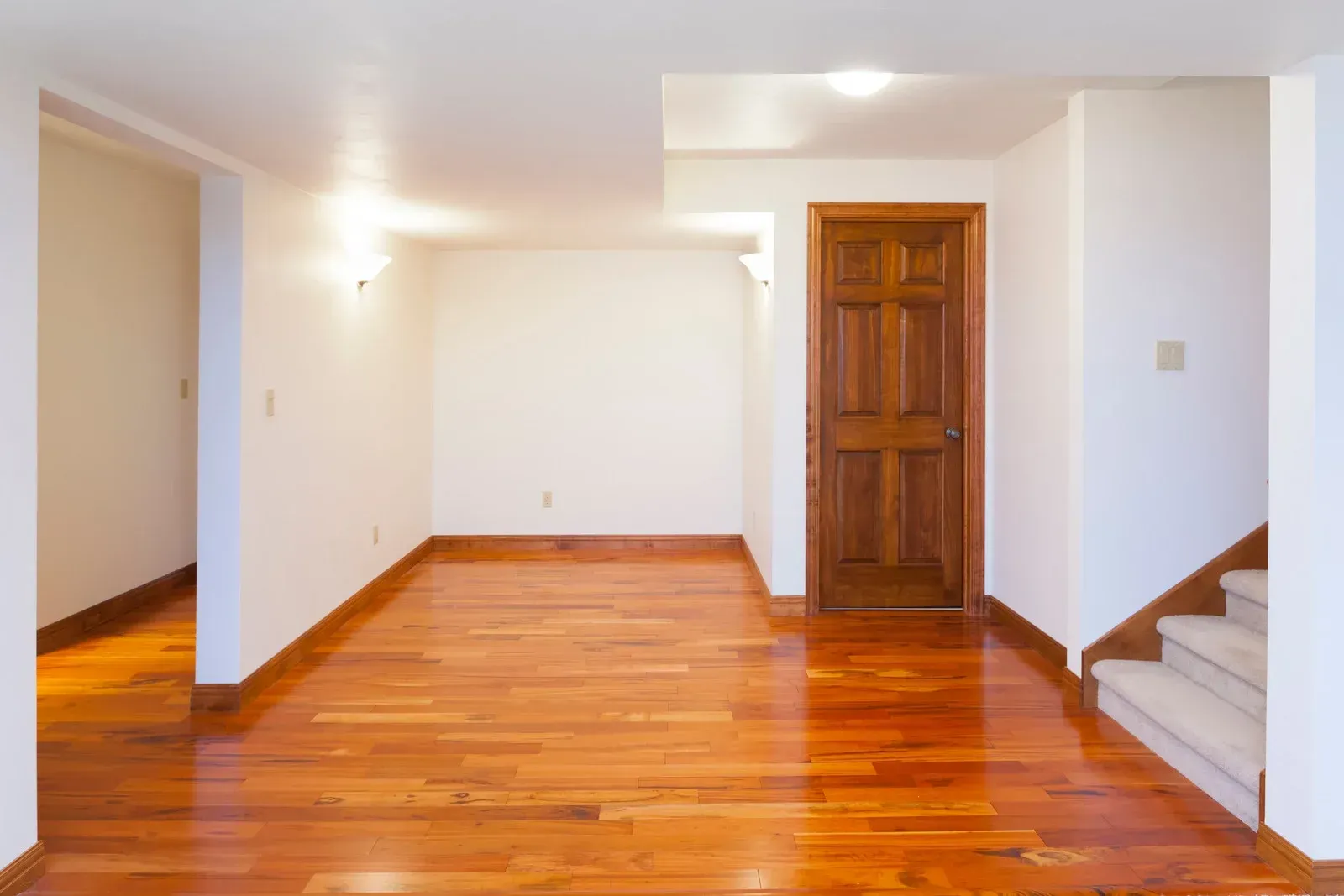 An empty basement with hardwood floors and white walls