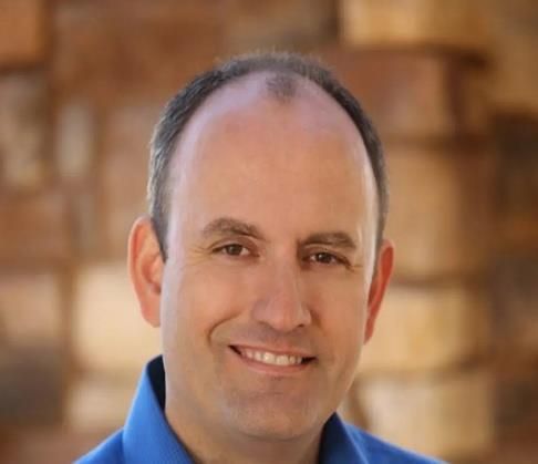 Smiling man in a blue shirt against a softly blurred warm-toned background