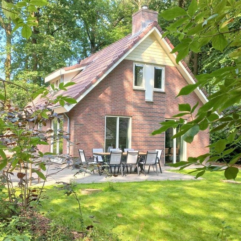 Bakstenen huis omgeven door bomen op een grindpad. Bewolkte dag.