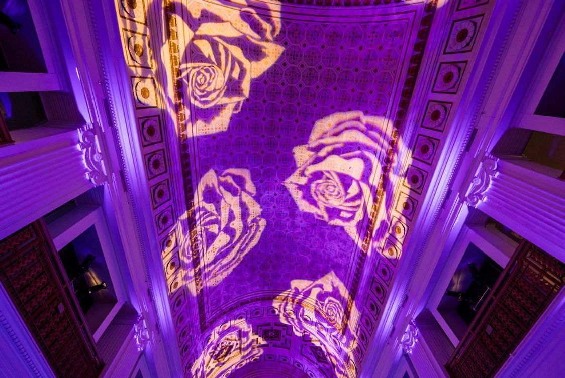 Purple-lit ornate ceiling with projected roses, viewed from below.