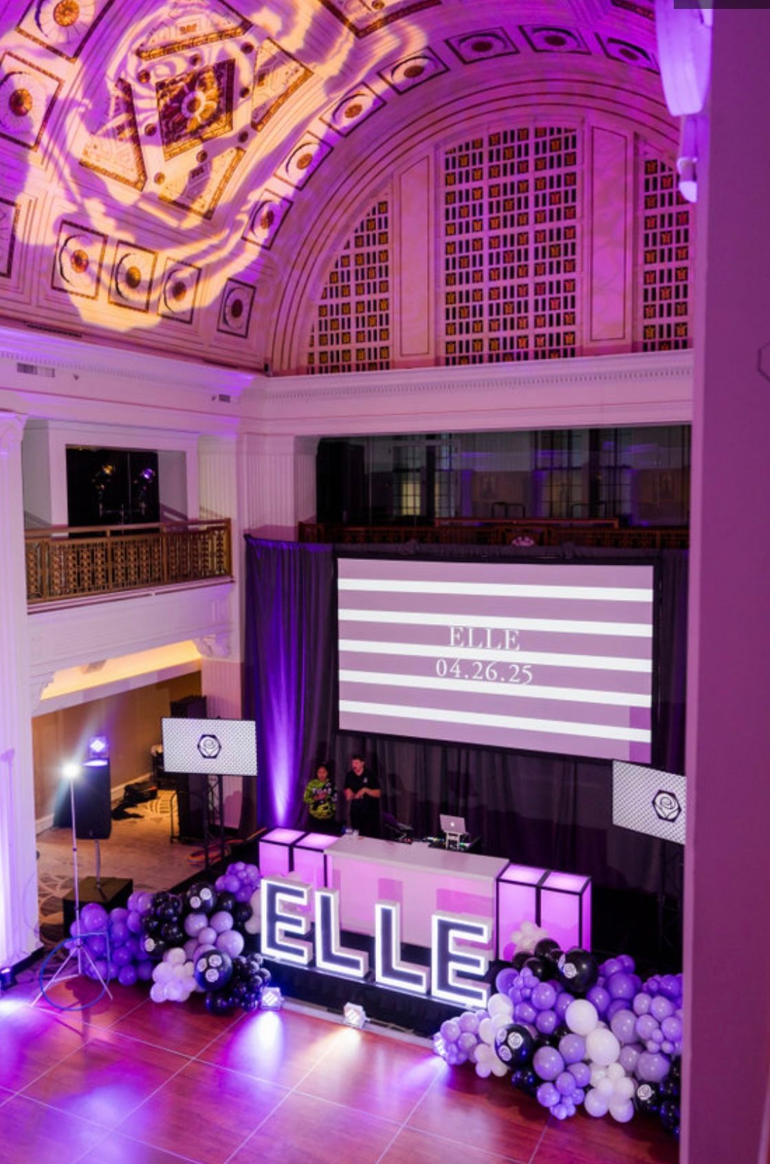 Event hall decorated in purple and white with a DJ setup. 
