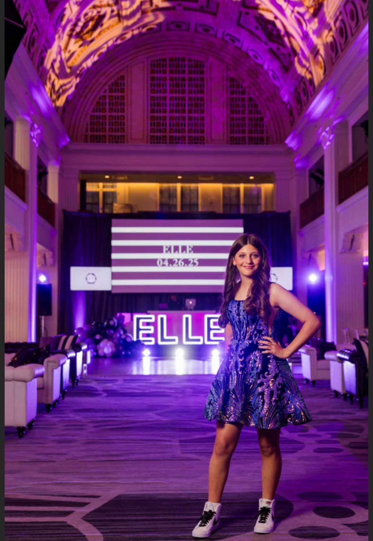 A girl in a blue sequined dress poses in front of a purple-lit event space.