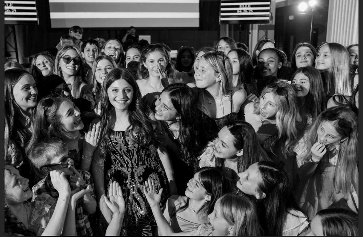 Group of young women smiling at camera; one centered woman wears a decorated dress.