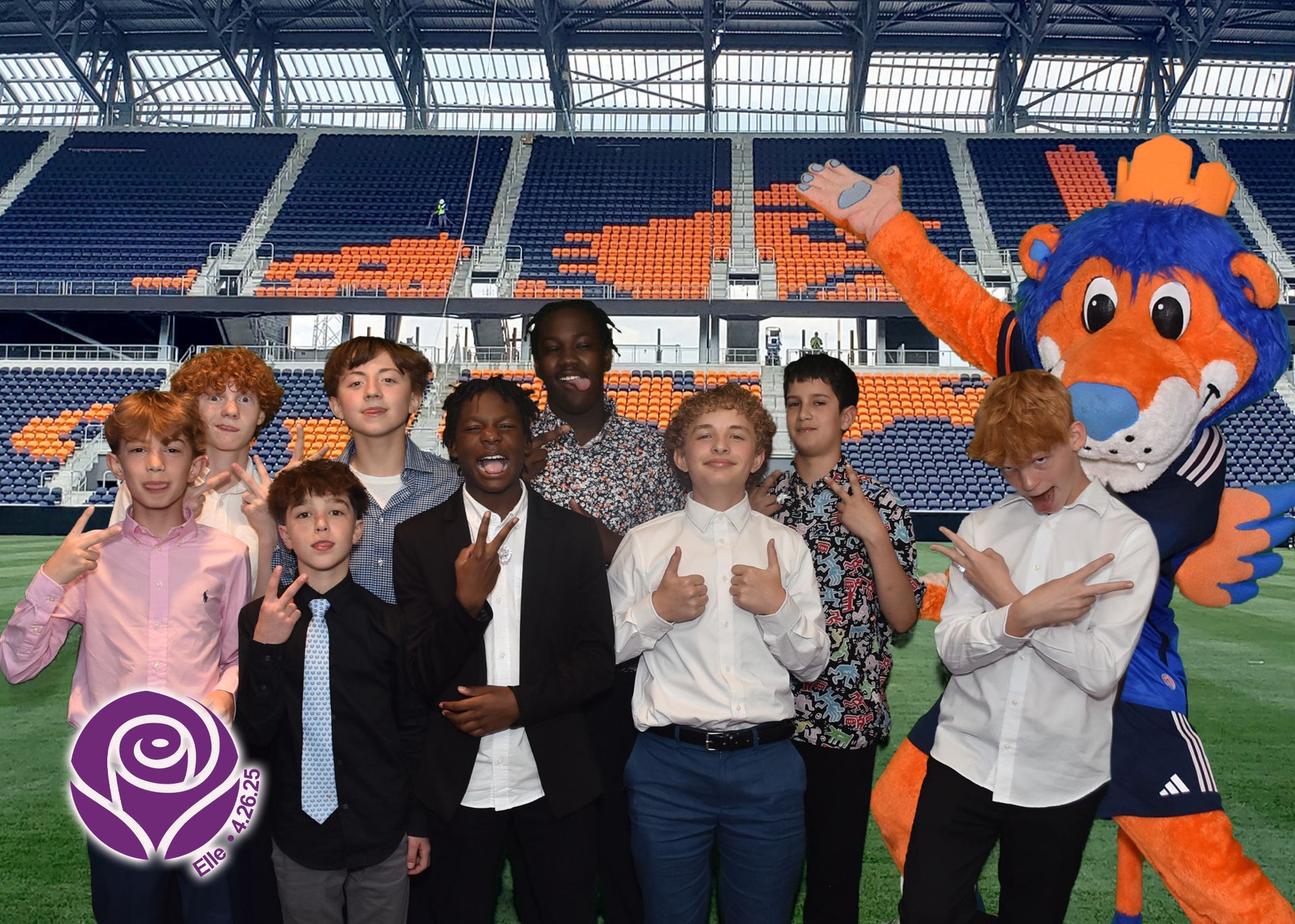 Group of teens and a mascot at a stadium, posing with hand gestures.