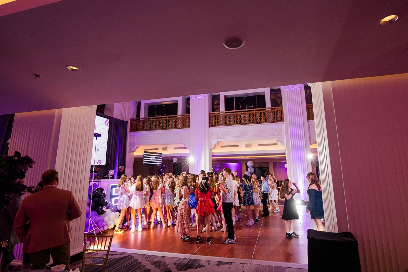 People dancing at a party in a brightly lit room with pink and purple hues.