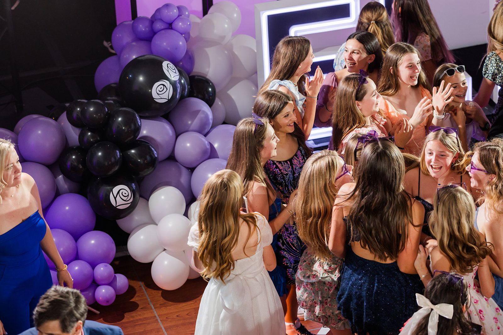 Group of girls at a party with purple, black, and white balloons. Some are taking pictures and smiling.