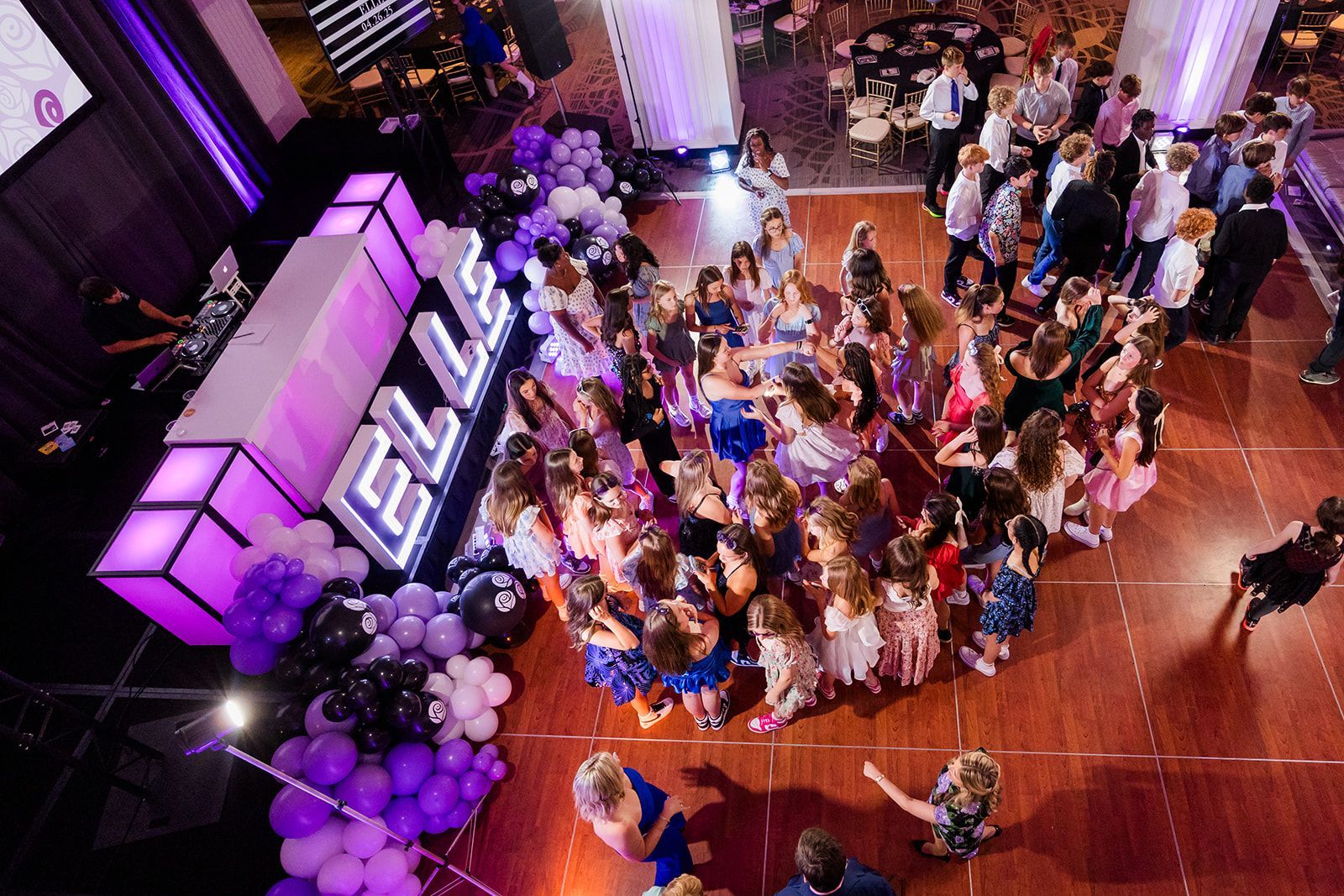 Overhead view of a party with many girls huddling in a circle on a dance floor, decorations, and event lights.