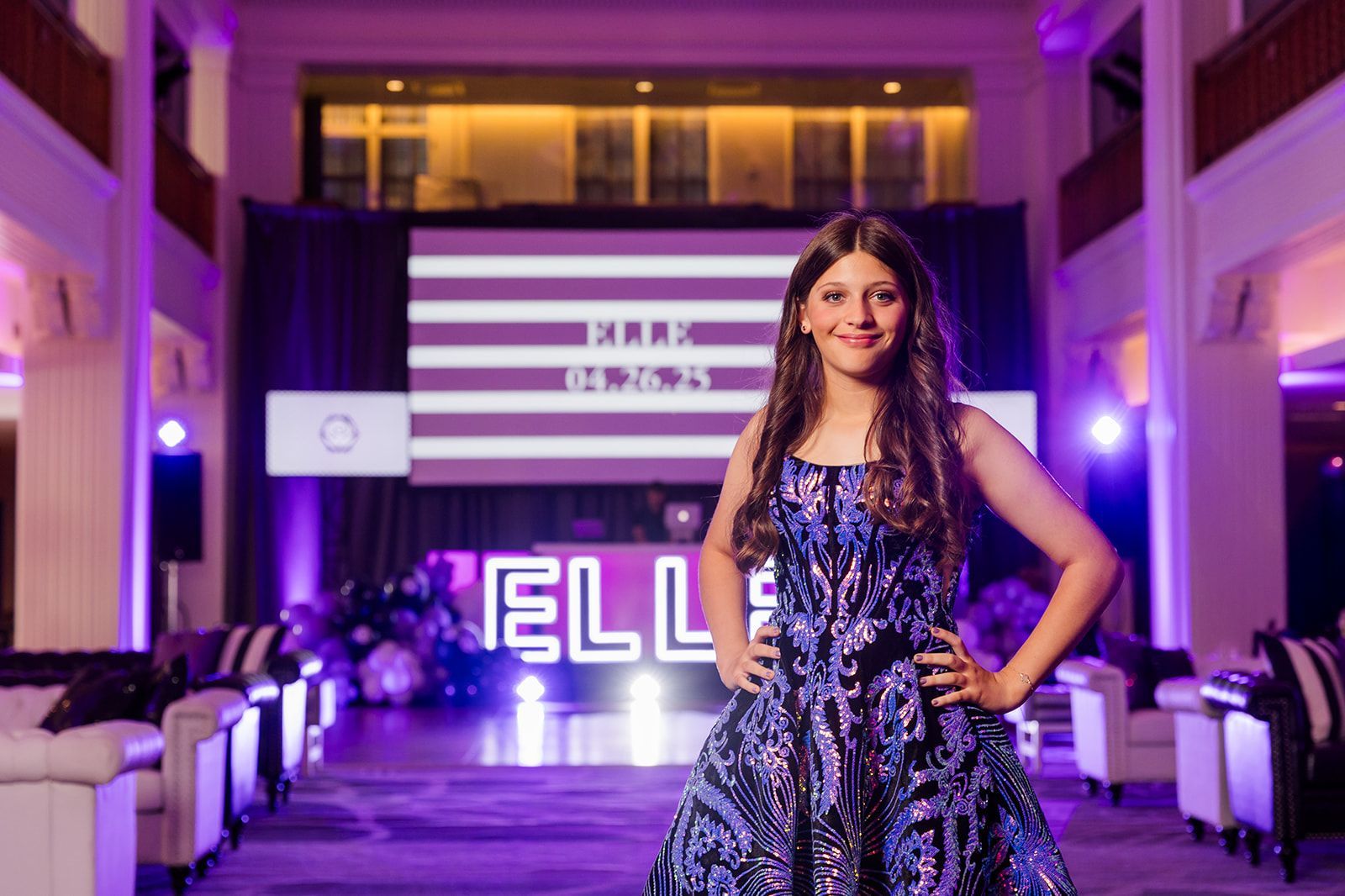 Girl in sparkly dress poses at birthday party, surrounded by purple lights and decorations.