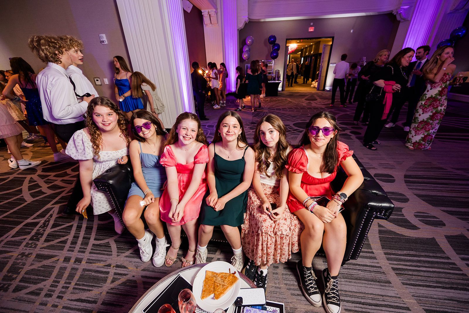 Group of smiling teens, diverse outfits, party setting with purple lighting.