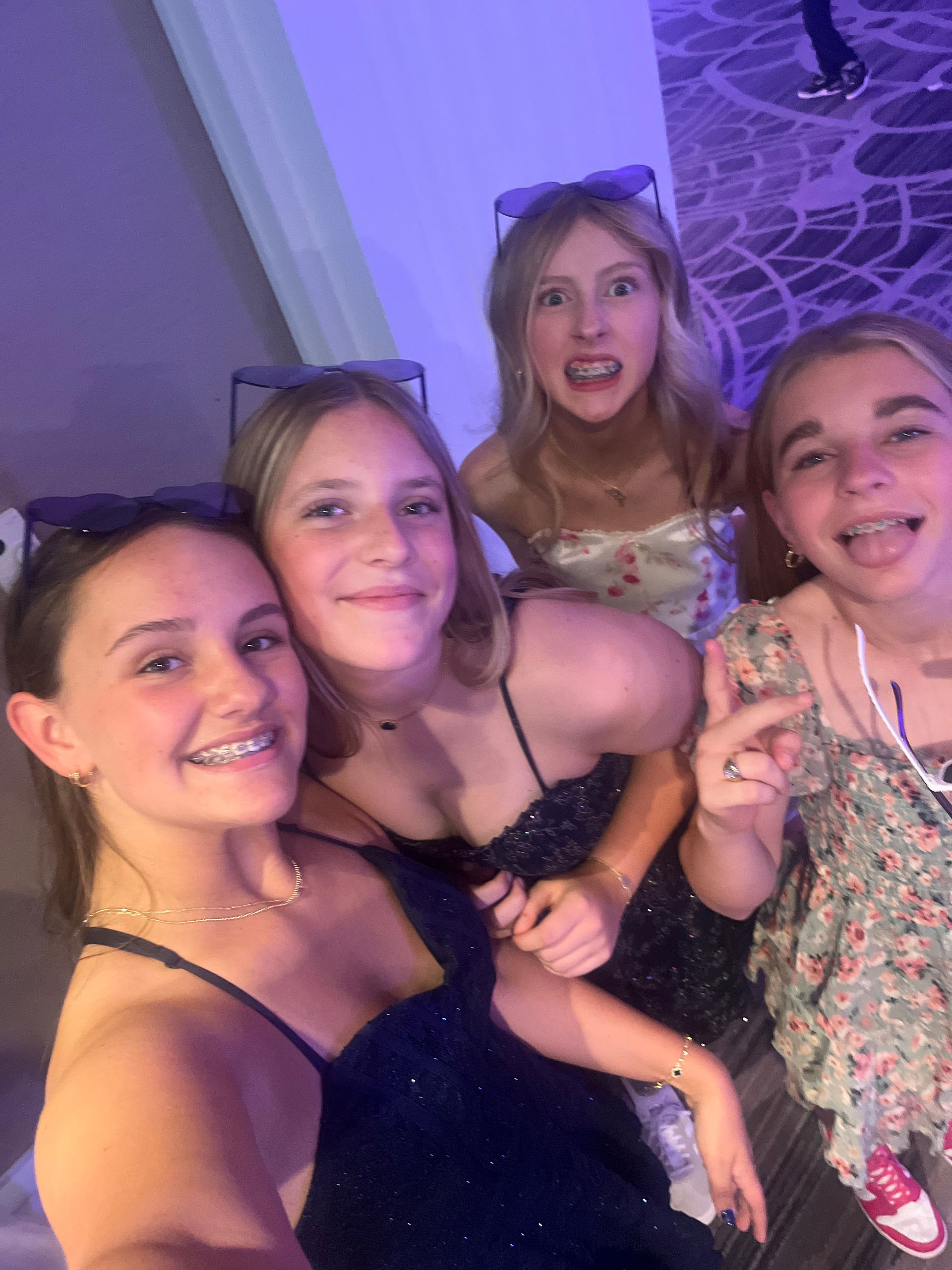 Four young women smiling and making faces at a formal event, lit with blue and white lights.