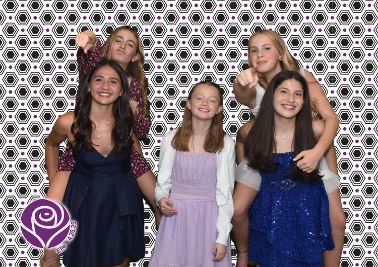 Six young women posing for a photo, against a geometric background. They are smiling and pointing.