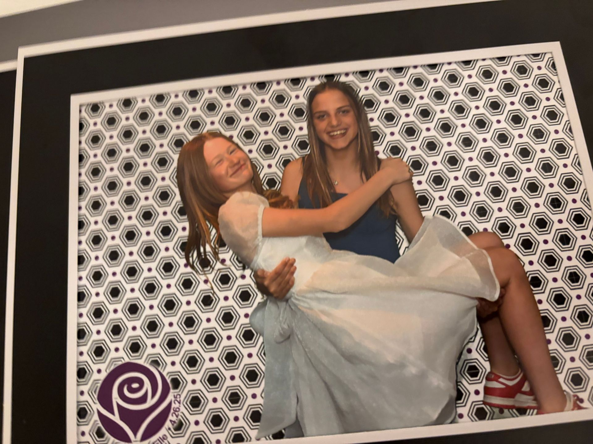 Two young women laughing, one carrying the other. Black and white patterned background.
