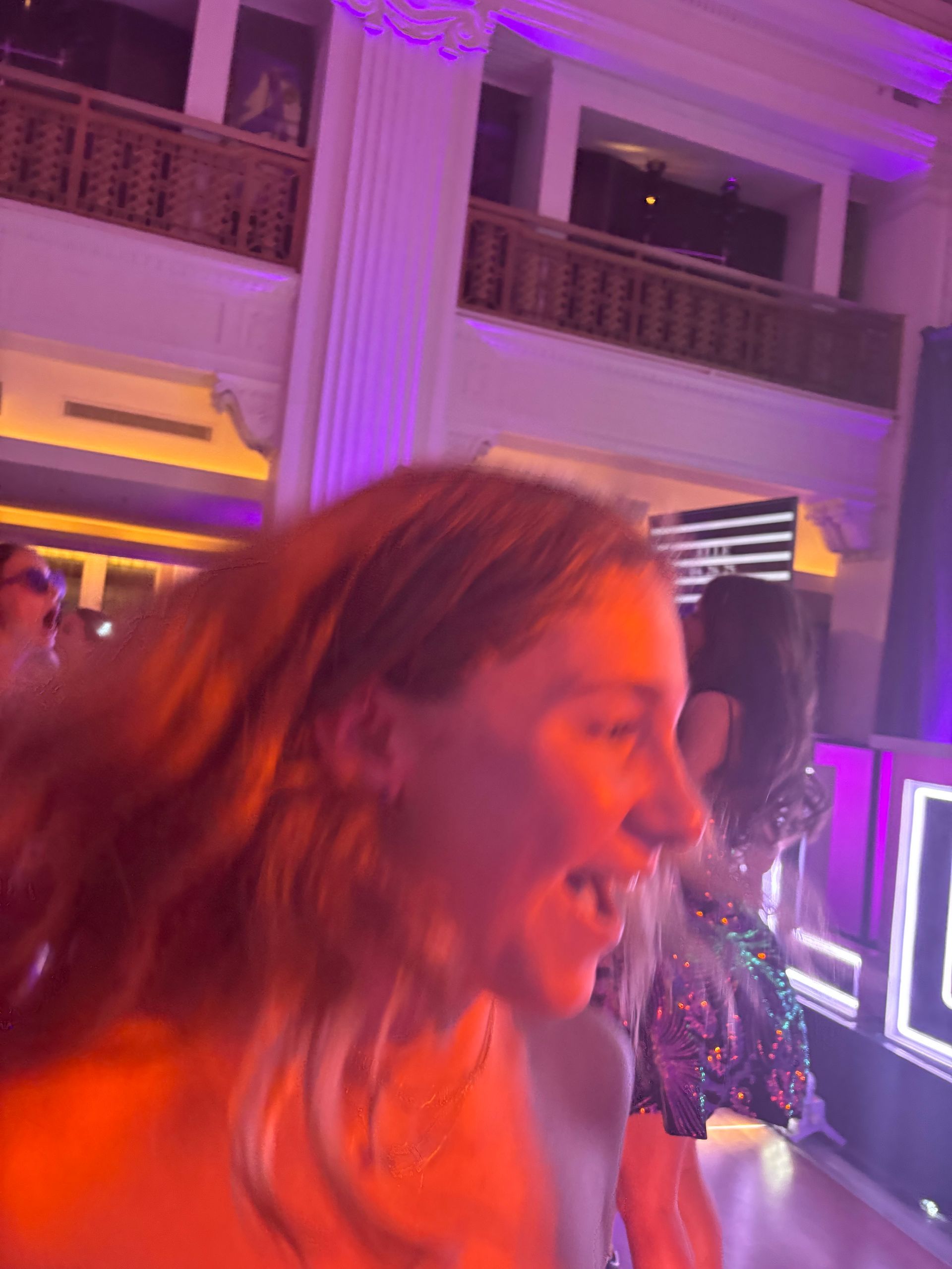 A woman with flowing red hair smiling at a party with bright pink lighting.