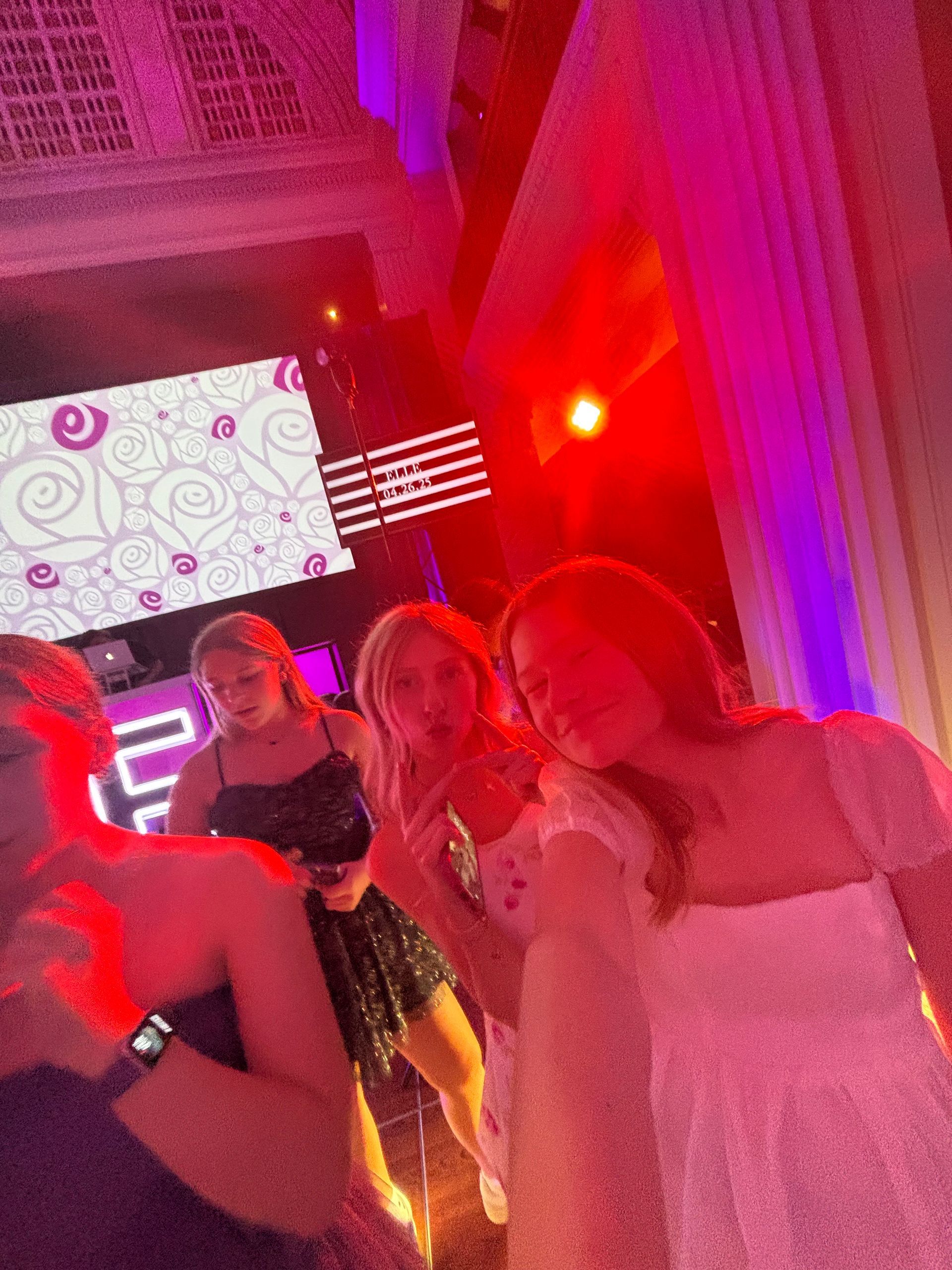 Four young people at a club, illuminated by red and purple lights. One person taking a selfie.