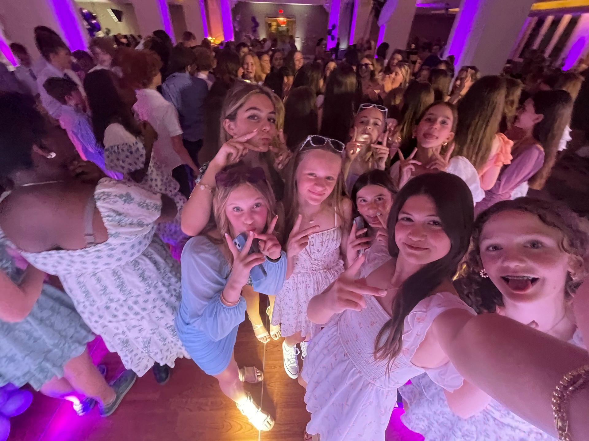 Teenagers at a dance, posing for a selfie. Many are smiling, holding up peace signs and looking at the camera.