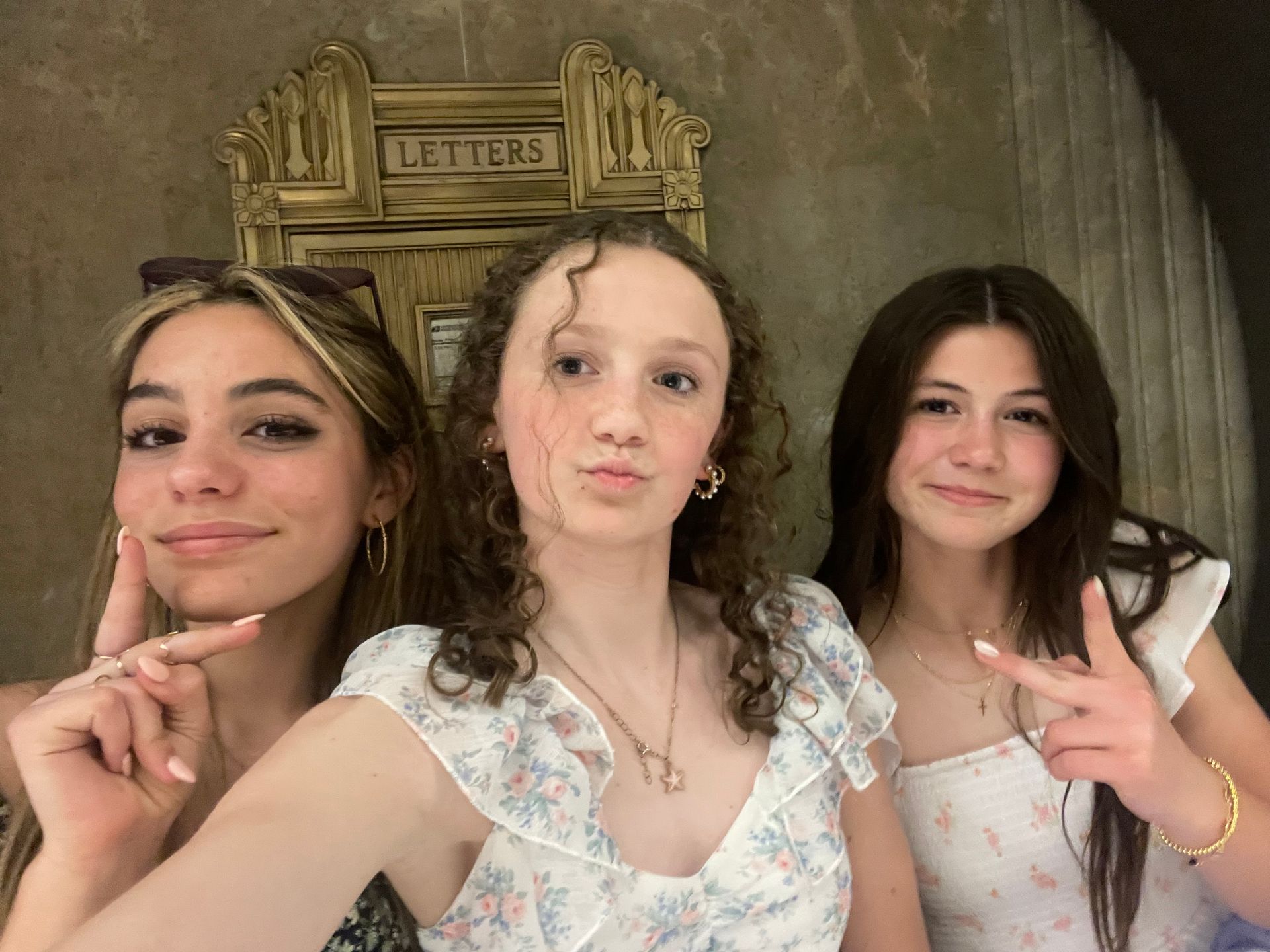 Three young women posing for a selfie. One makes a peace sign, another pouts, and the third points up.