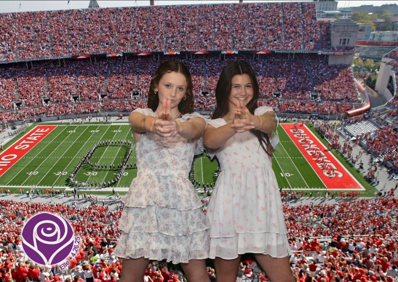 Two women in white dresses making hand gestures at Ohio State football stadium.