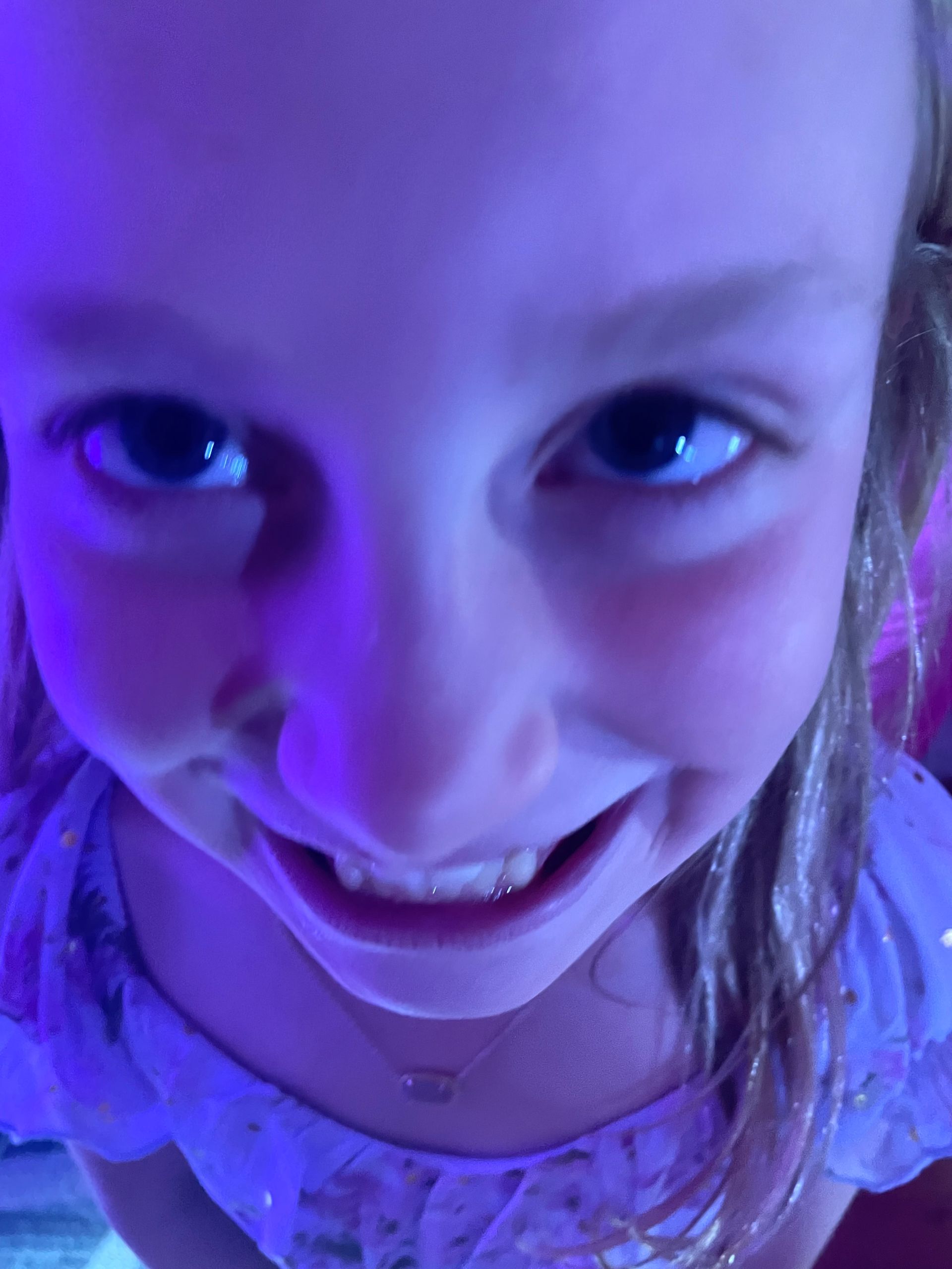 Girl smiles up at the camera, under blue light.