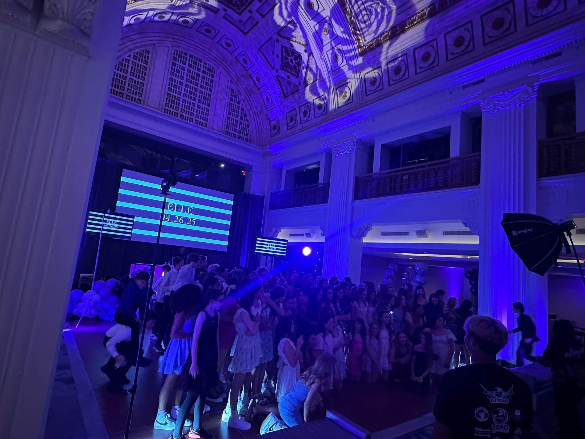 Large event with people dancing under blue lights, projected art on ceiling.