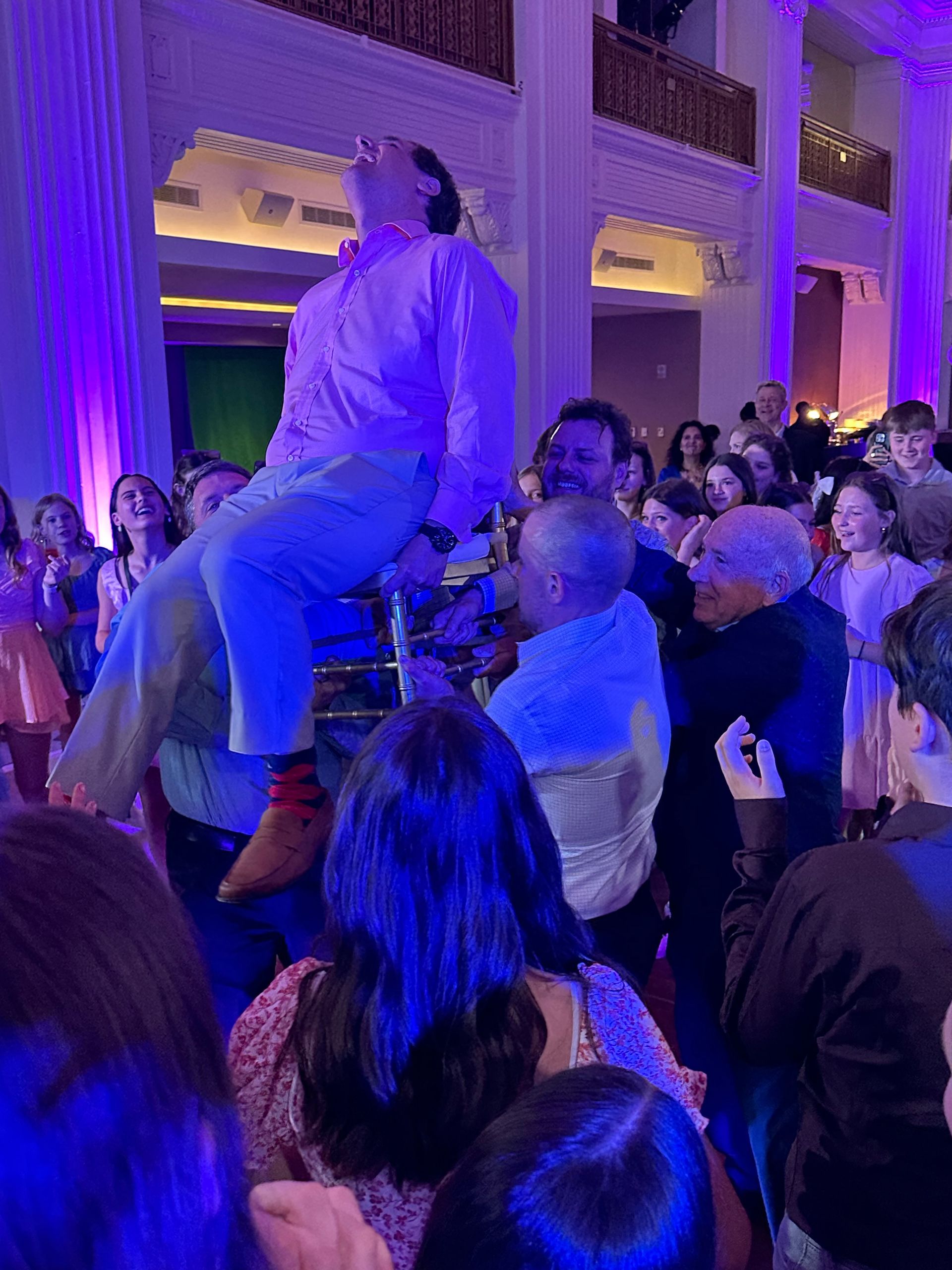 Man being lifted up in the air by a crowd, likely at a celebration. He is smiling and appears joyful.