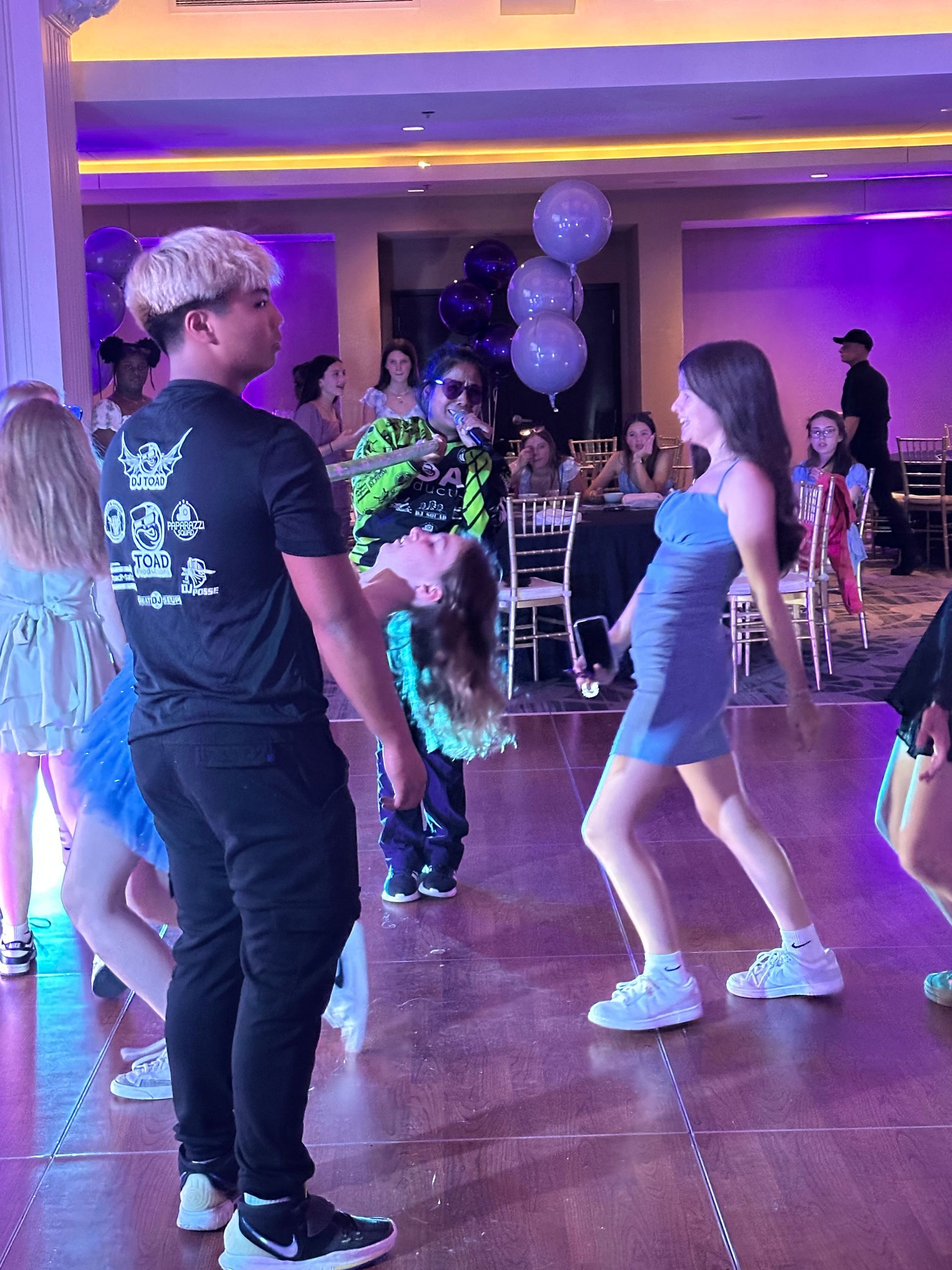 People dancing at a party with purple lighting, one person being flipped in the air.