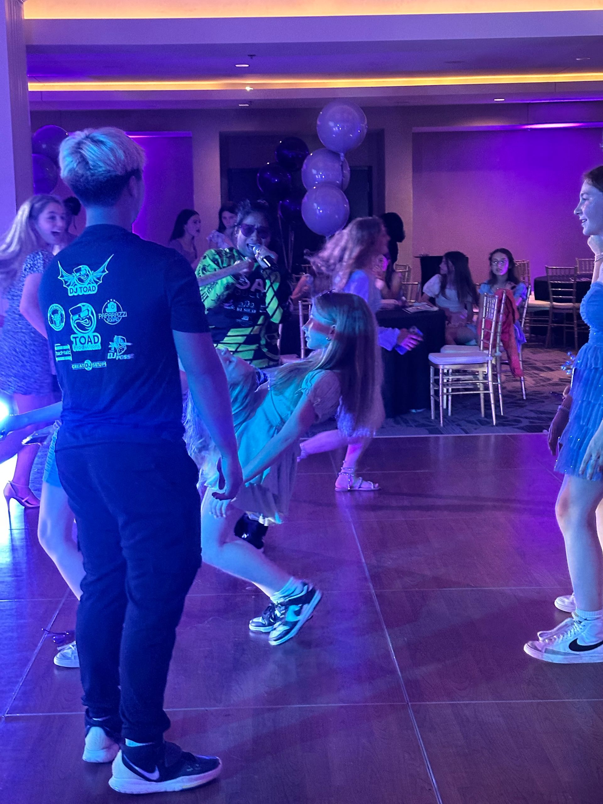 Teenagers dancing on a lit dance floor with purple and white lights.