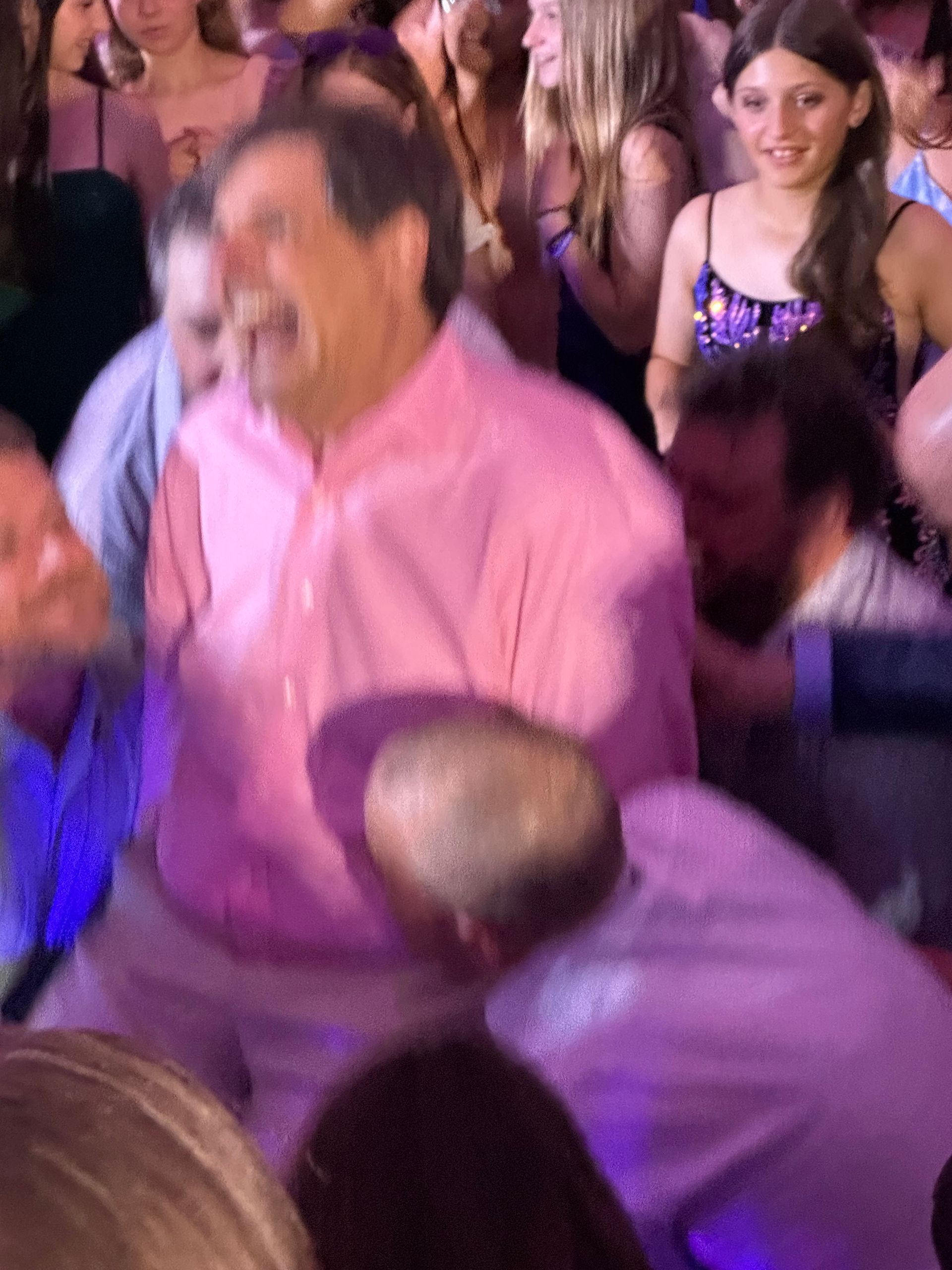 Man in pink shirt laughing in a crowd, likely at a party or event.