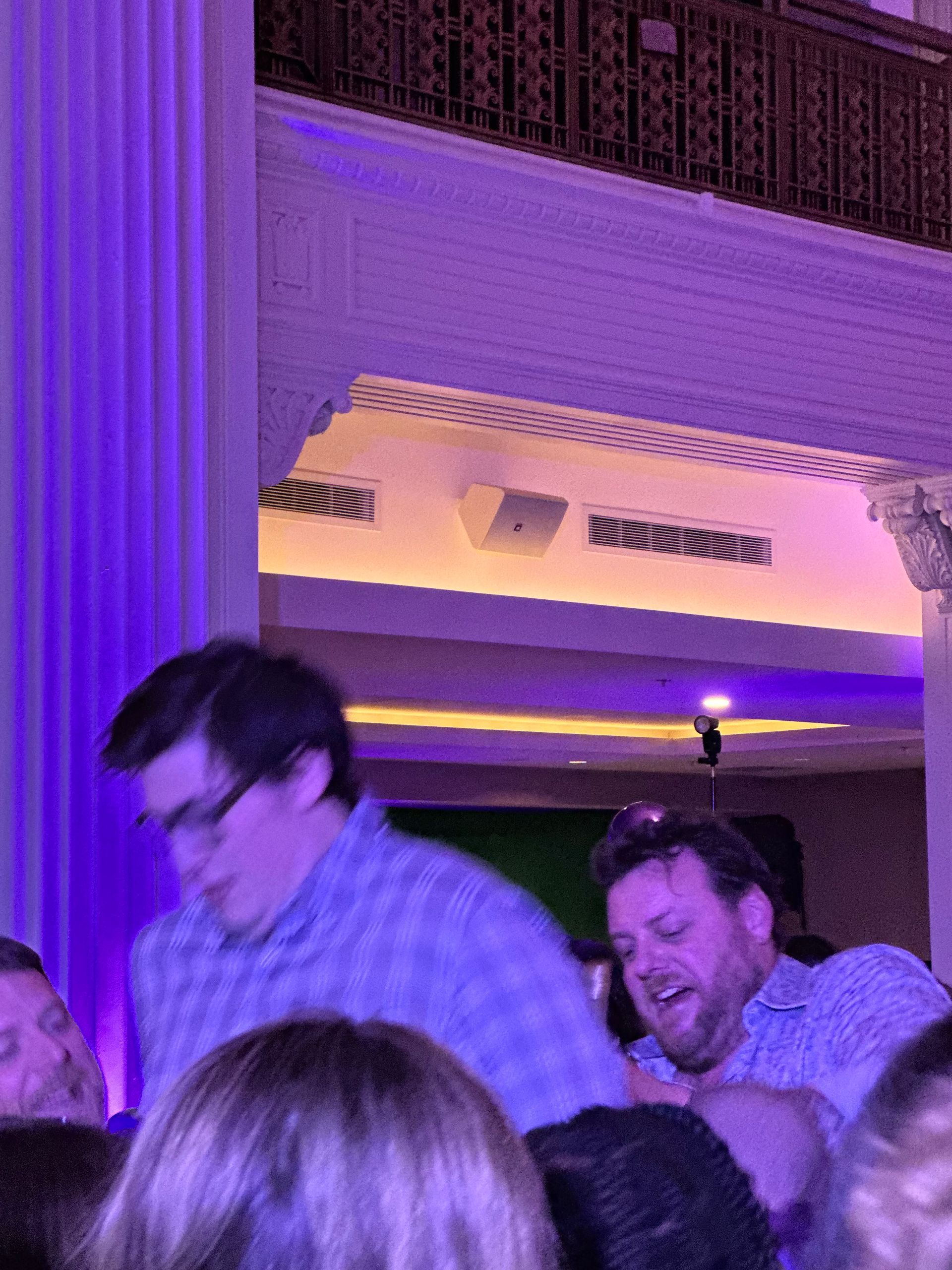 Two men appear to be playfully struggling, surrounded by people in a room with purple lighting.