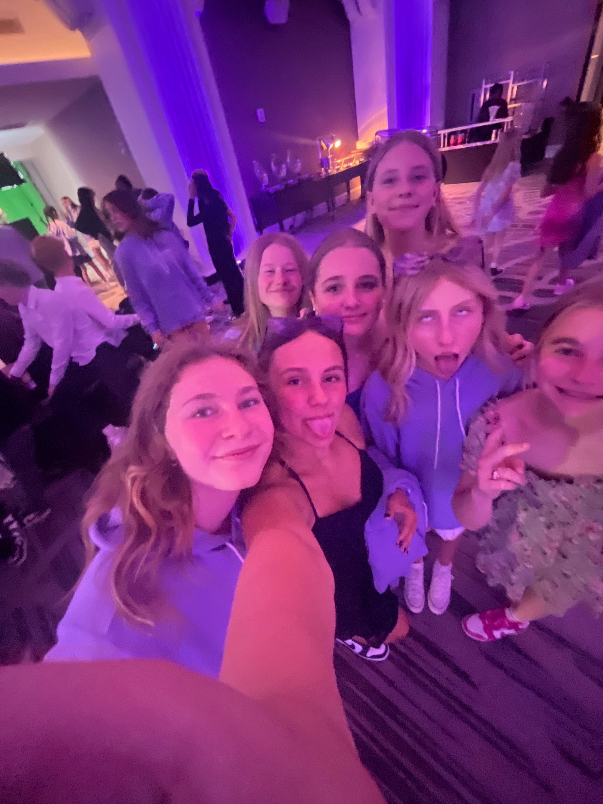 Group of girls taking a selfie at a party with purple lighting. They are smiling and making faces.