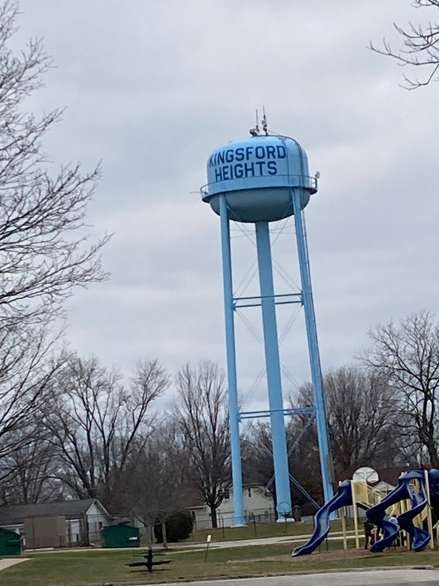 A water tower in a park with a playground in the background.