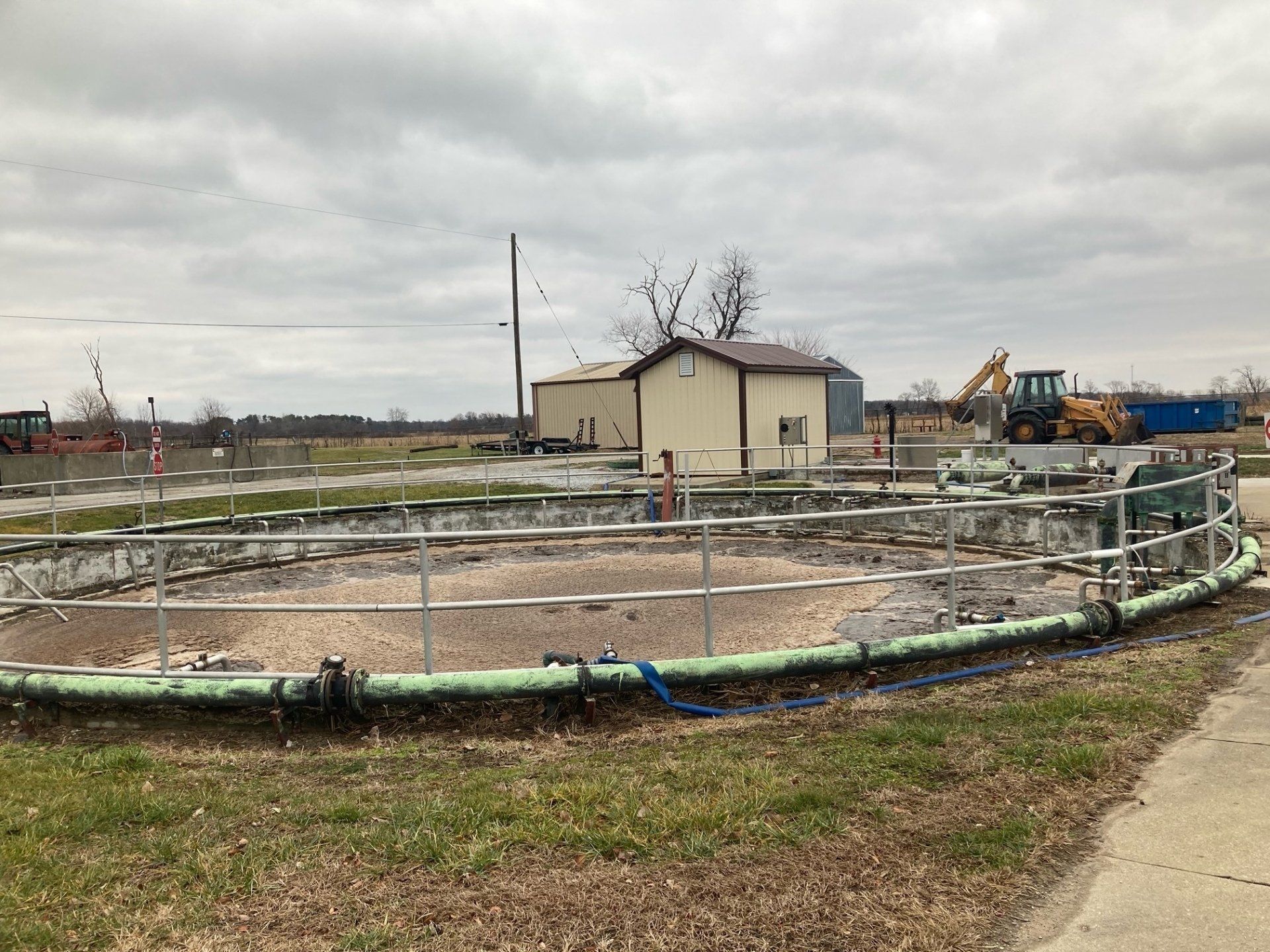 A large circular pond with a fence around it and a building in the background.