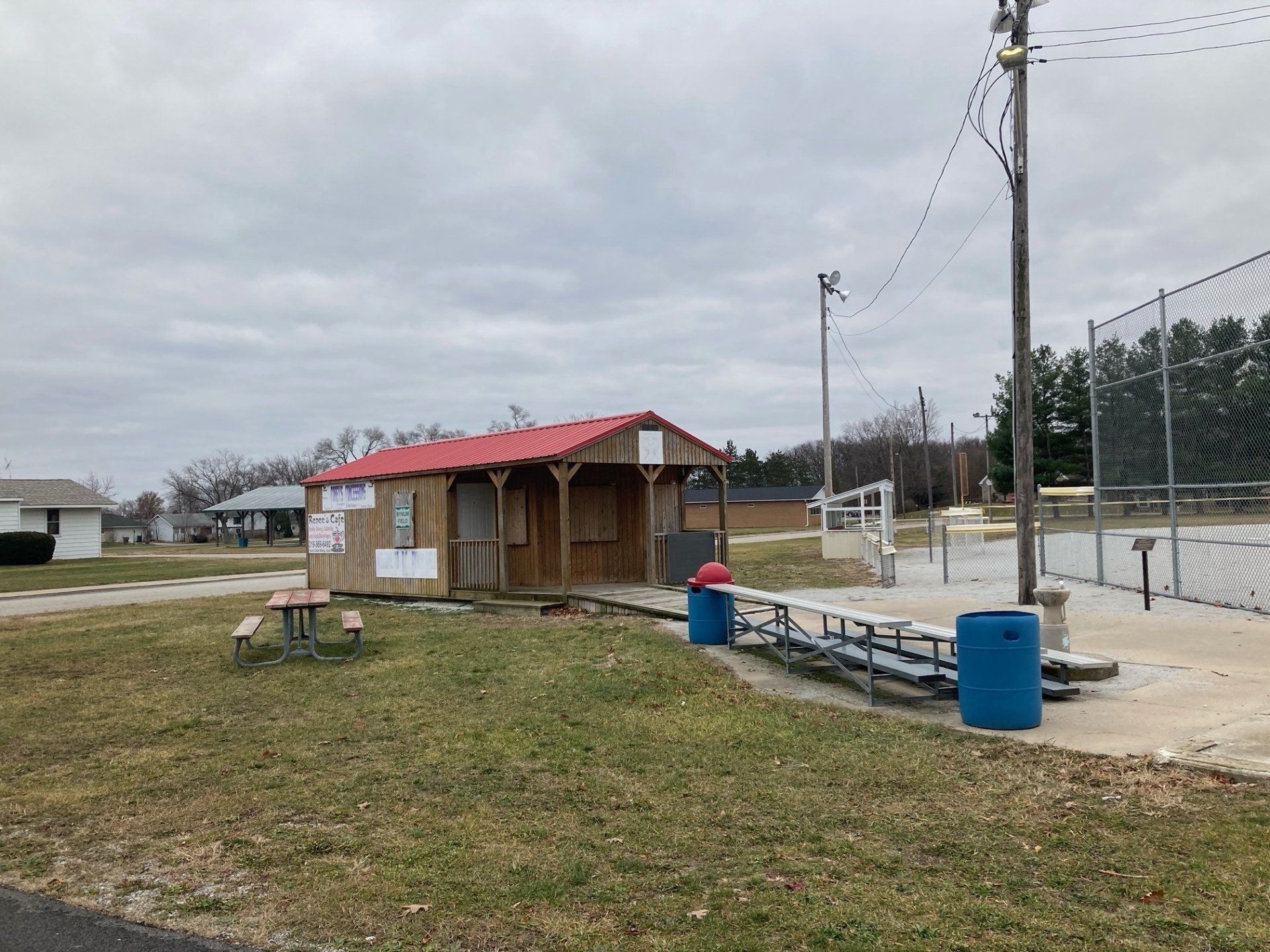 A small wooden building with a red roof is sitting in the middle of a grassy field.