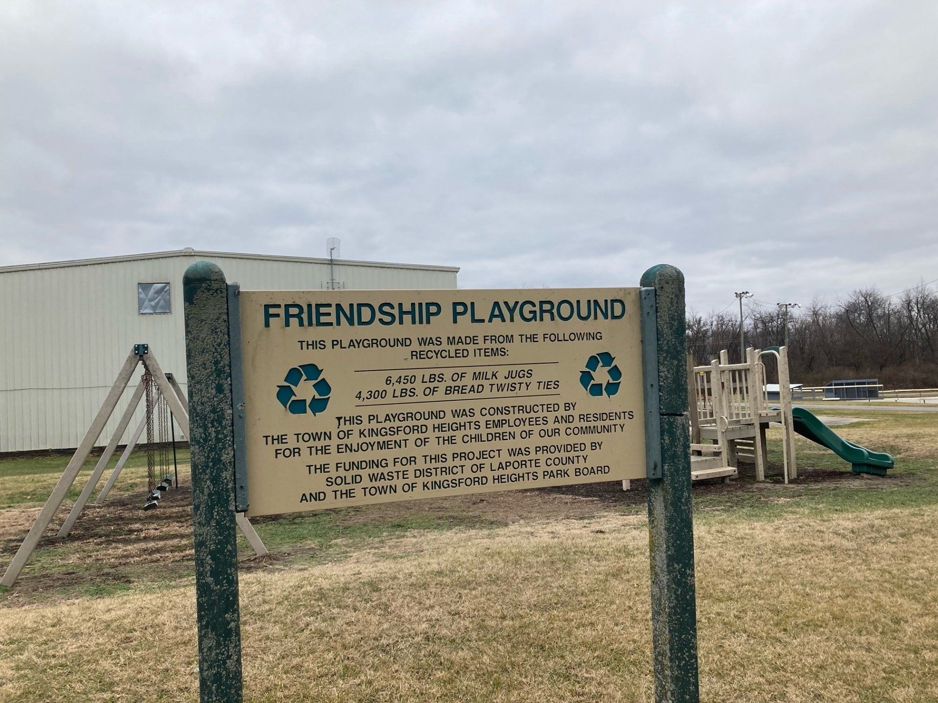 A sign for the friendship playground is in front of a playground.