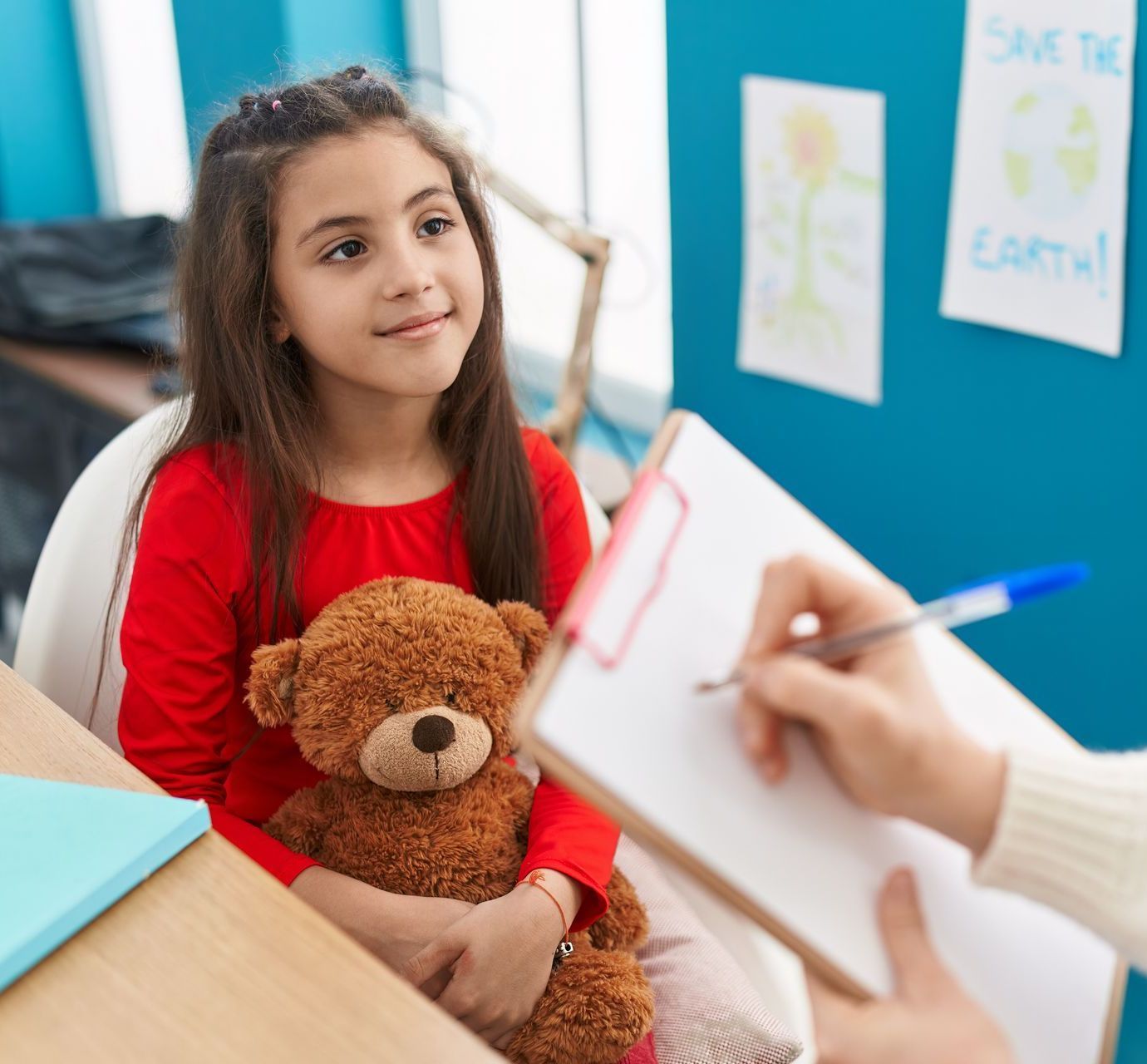 A little girl is holding a teddy bear and talking to a therapist.