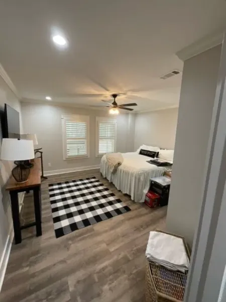 A bedroom with two beds , a checkered rug , a ceiling fan and a television.
