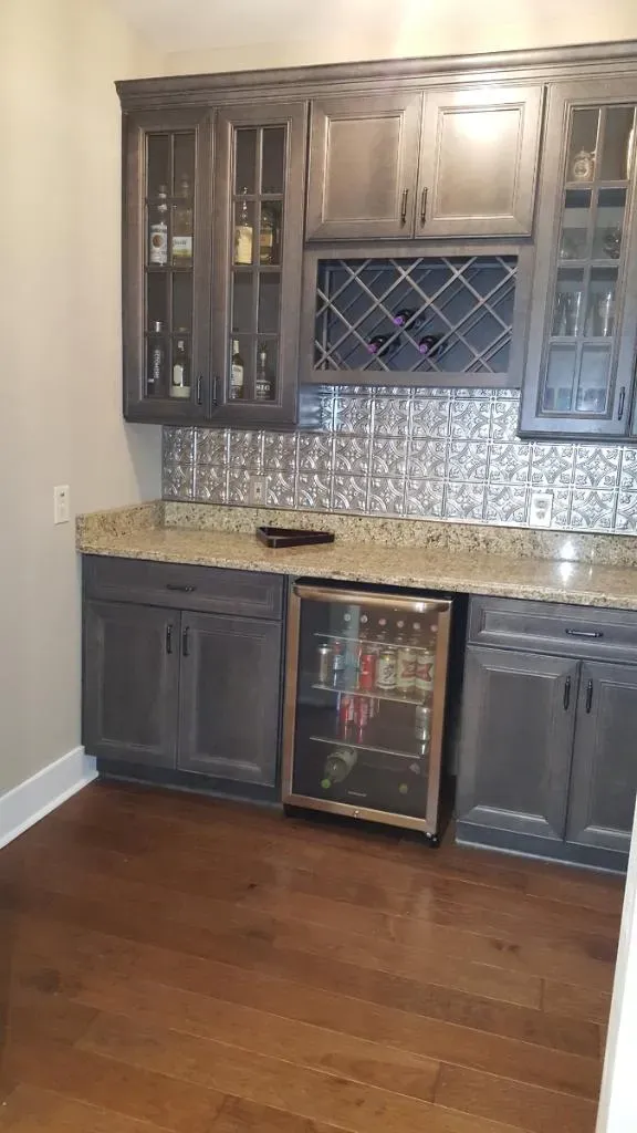 A kitchen with gray cabinets , granite counter tops , and a wine cooler.