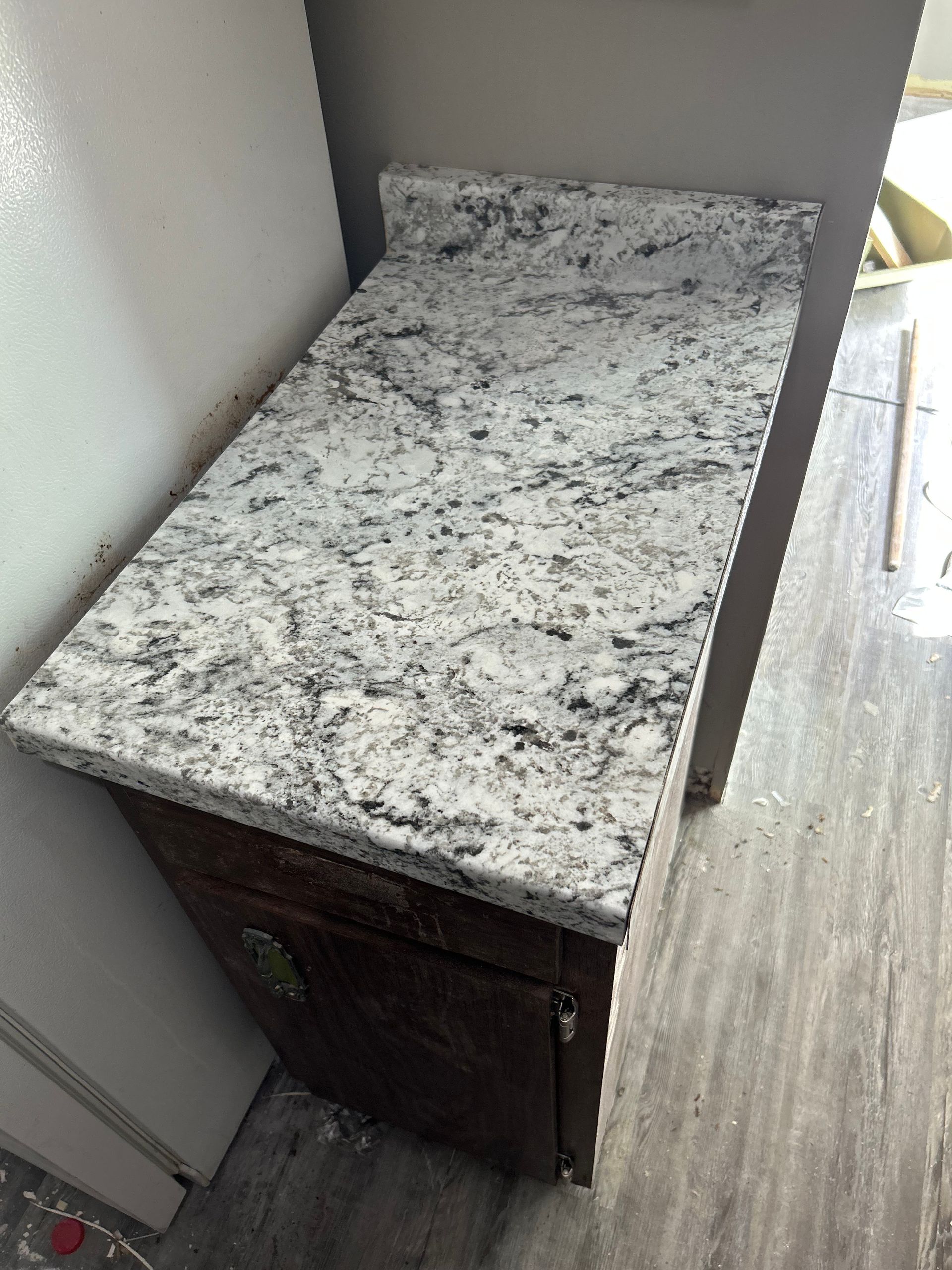 Countertop with white and gray speckled design on a dark brown cabinet.